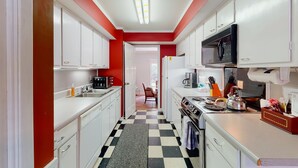 A narrow kitchen with white cabinets, a black and white checkered floor, and a red accent wall. - Condo With Central AC, Washer/dryer, Shared Outdoor Pool, & On-site Golf (St. Simons Island)