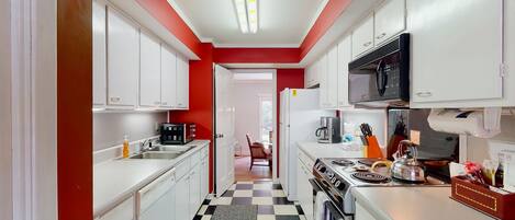 Une cuisine étroite avec des meubles blancs, un carrelage noir et blanc et un mur d’accent rouge.