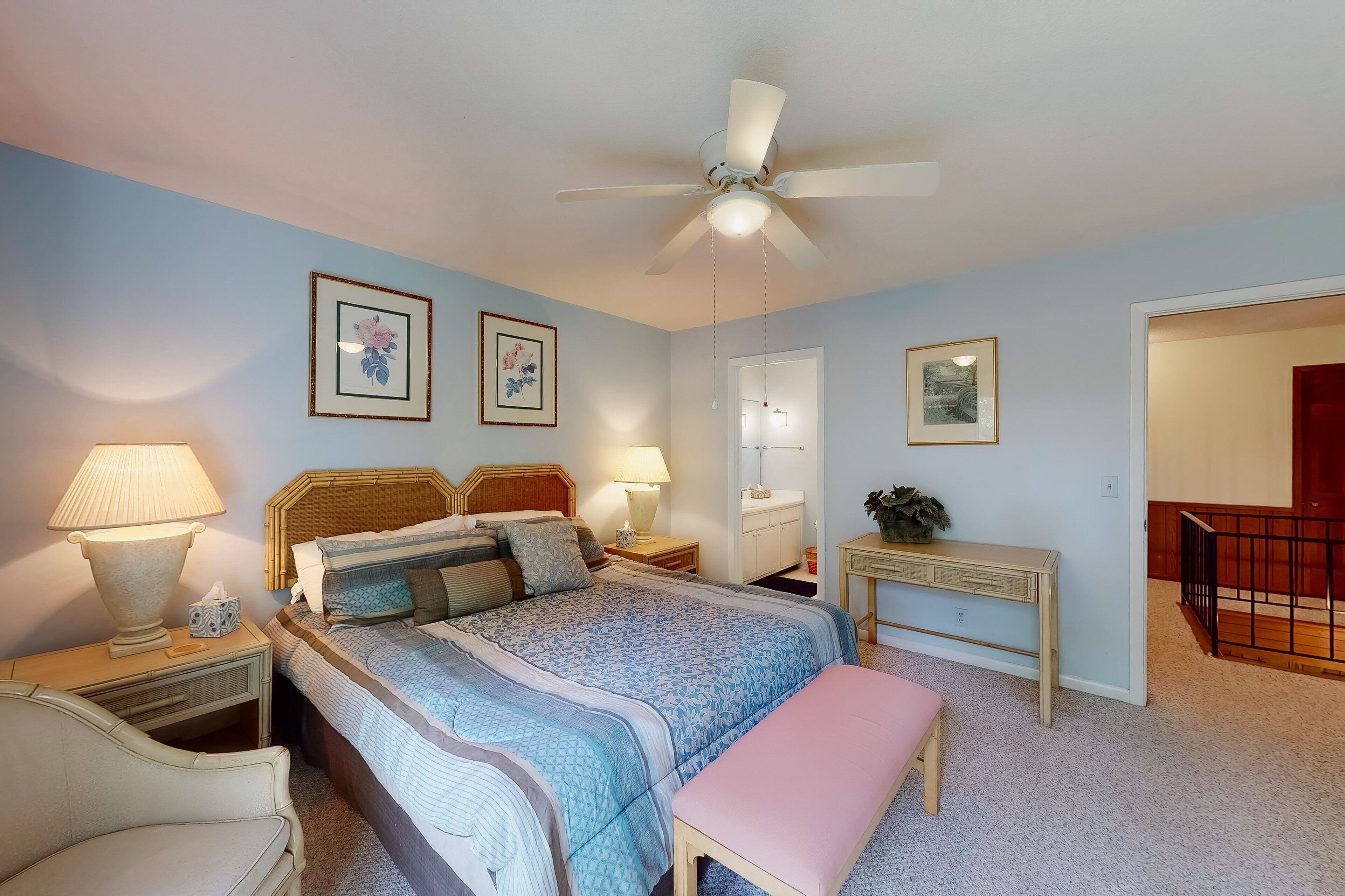 A bedroom with a bed, bedside tables, a desk, a chair, a bench, and a ceiling fan.