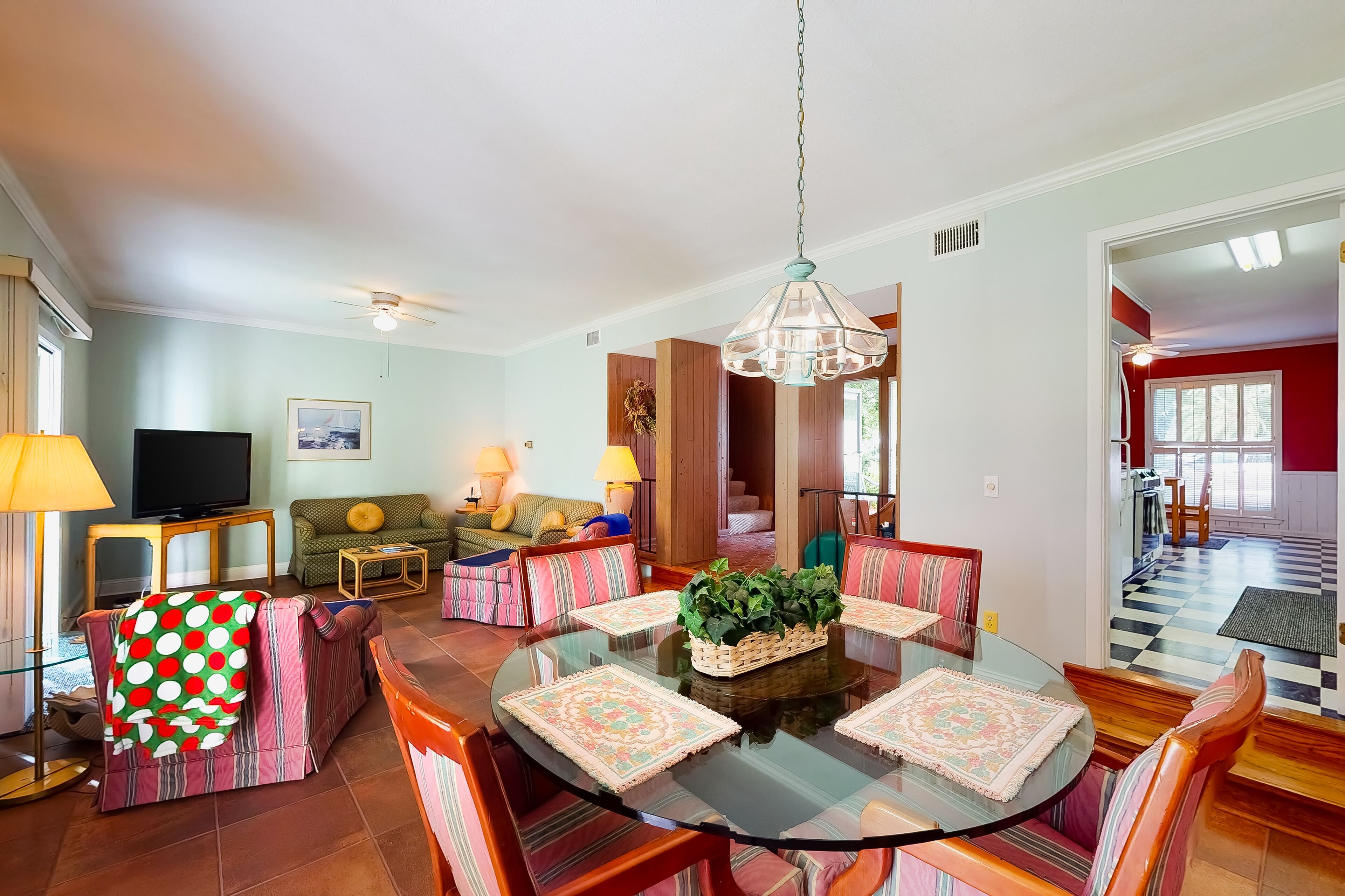 A spacious living room with a round glass table, striped chairs, a television, and a ceiling fan.
