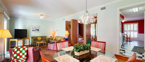A spacious living room with a round glass table, striped chairs, a television, and a ceiling fan.