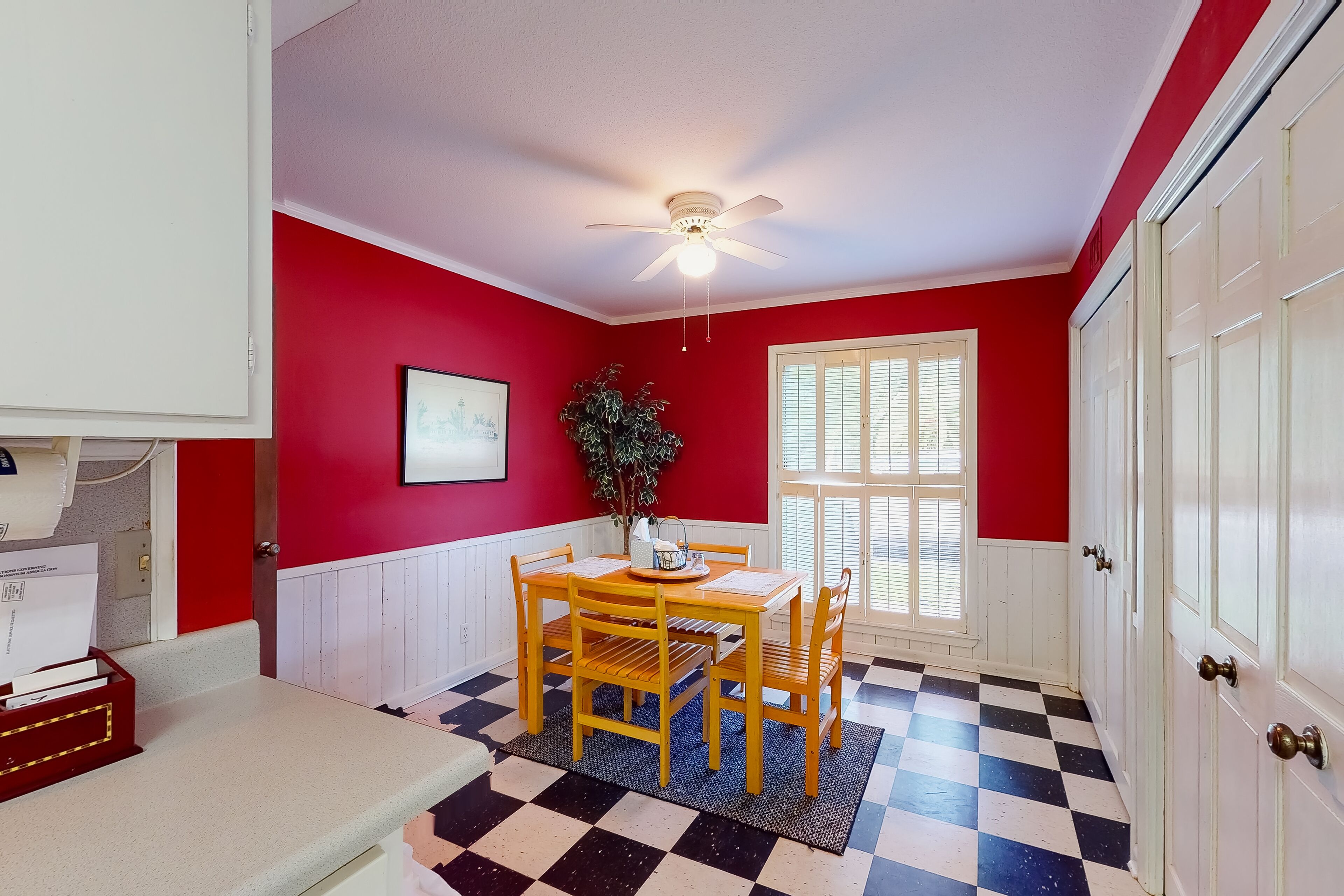A dining area with a checkered floor, red walls, and a ceiling fan.