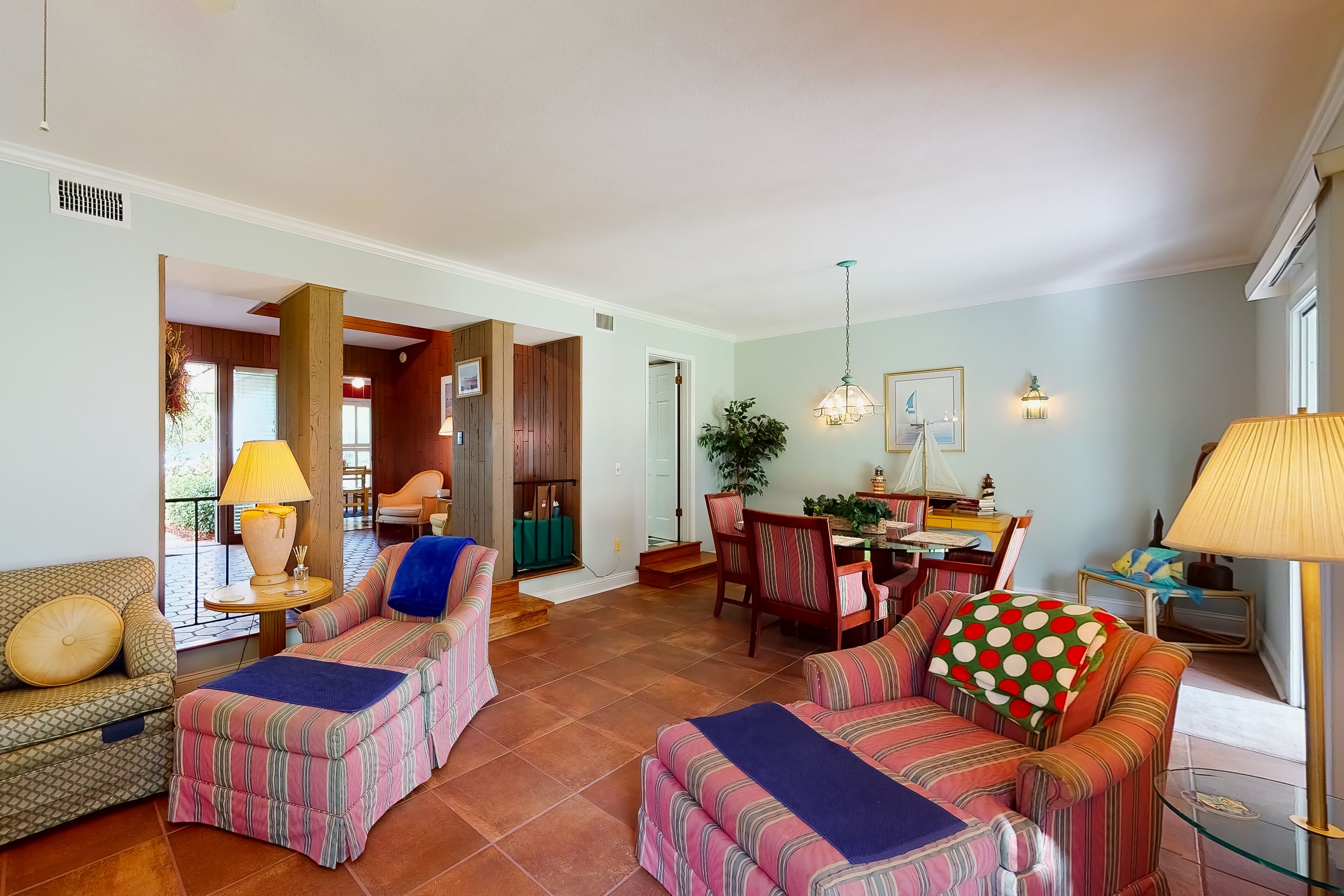 A spacious living room with a dining area, featuring a large window, a chandelier, and a variety of seating options.