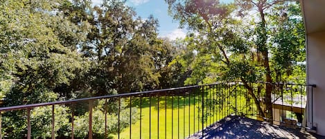 A balcony with a metal railing overlooking a grassy area with trees.