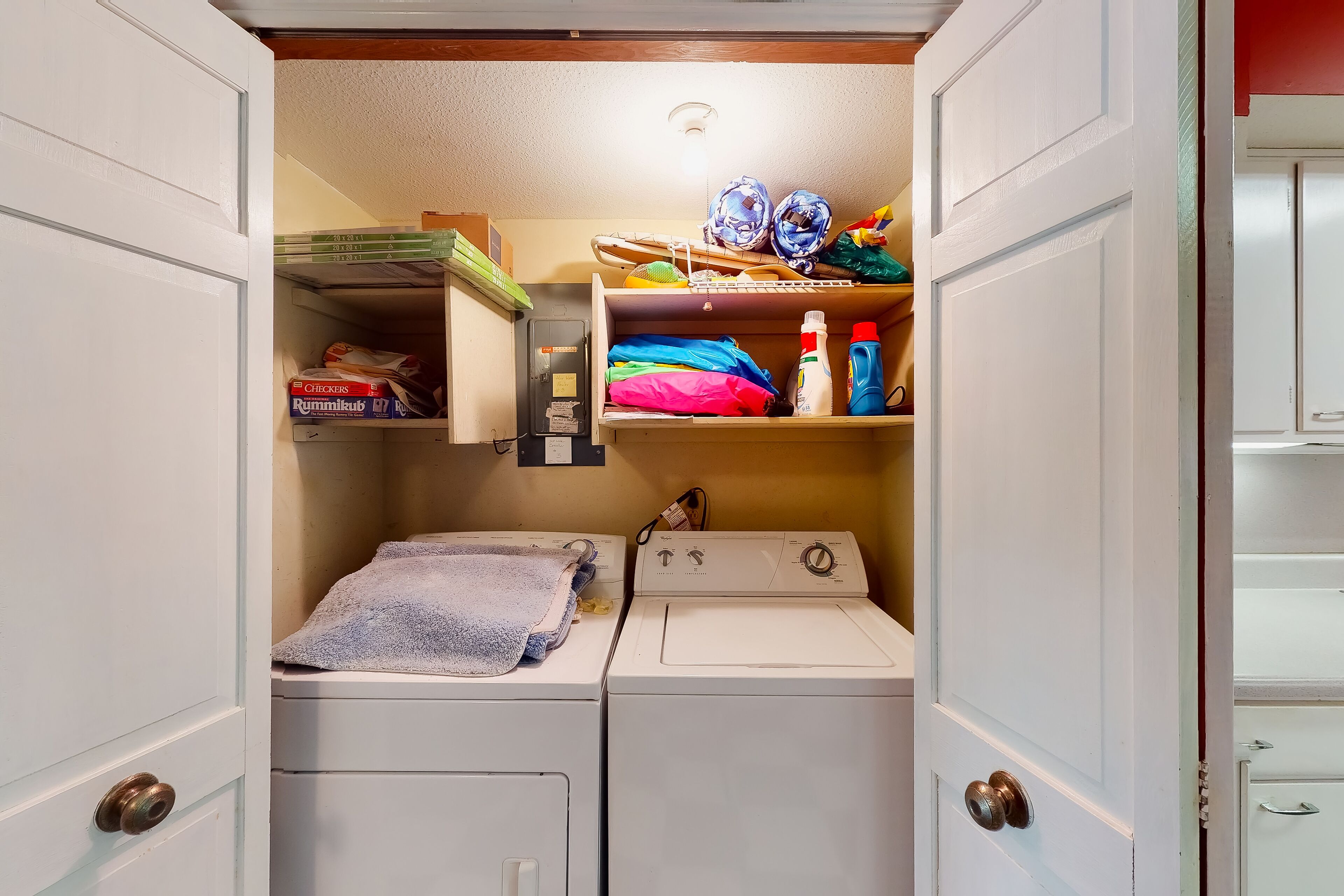 Une buanderie équipée d’un lave-linge et d’un sèche-linge, de plusieurs étagères contenant des produits de nettoyage et d’une petite étagère avec des livres.