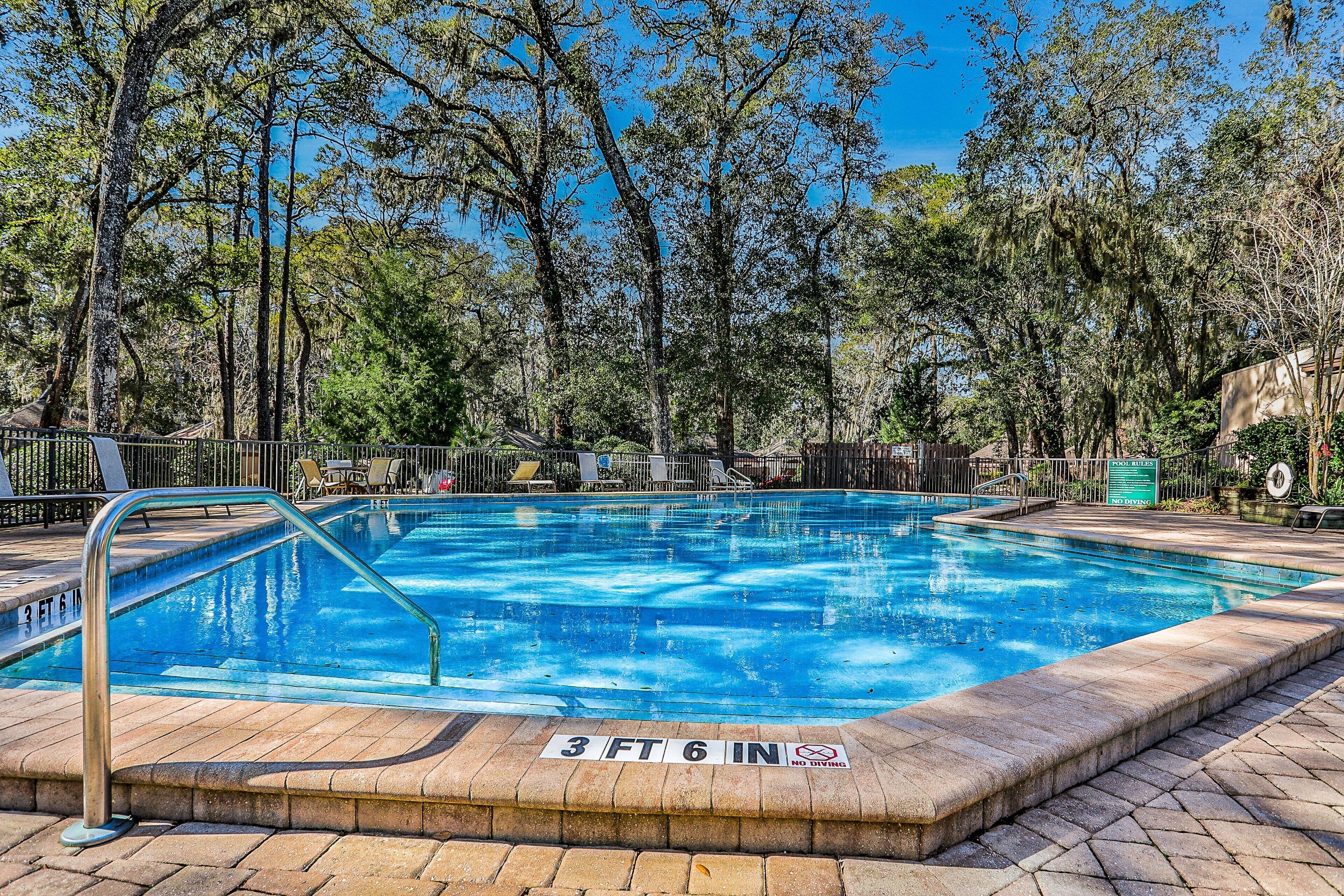 A rectangular swimming pool with a metal ladder, surrounded by a brick deck and a metal fence.