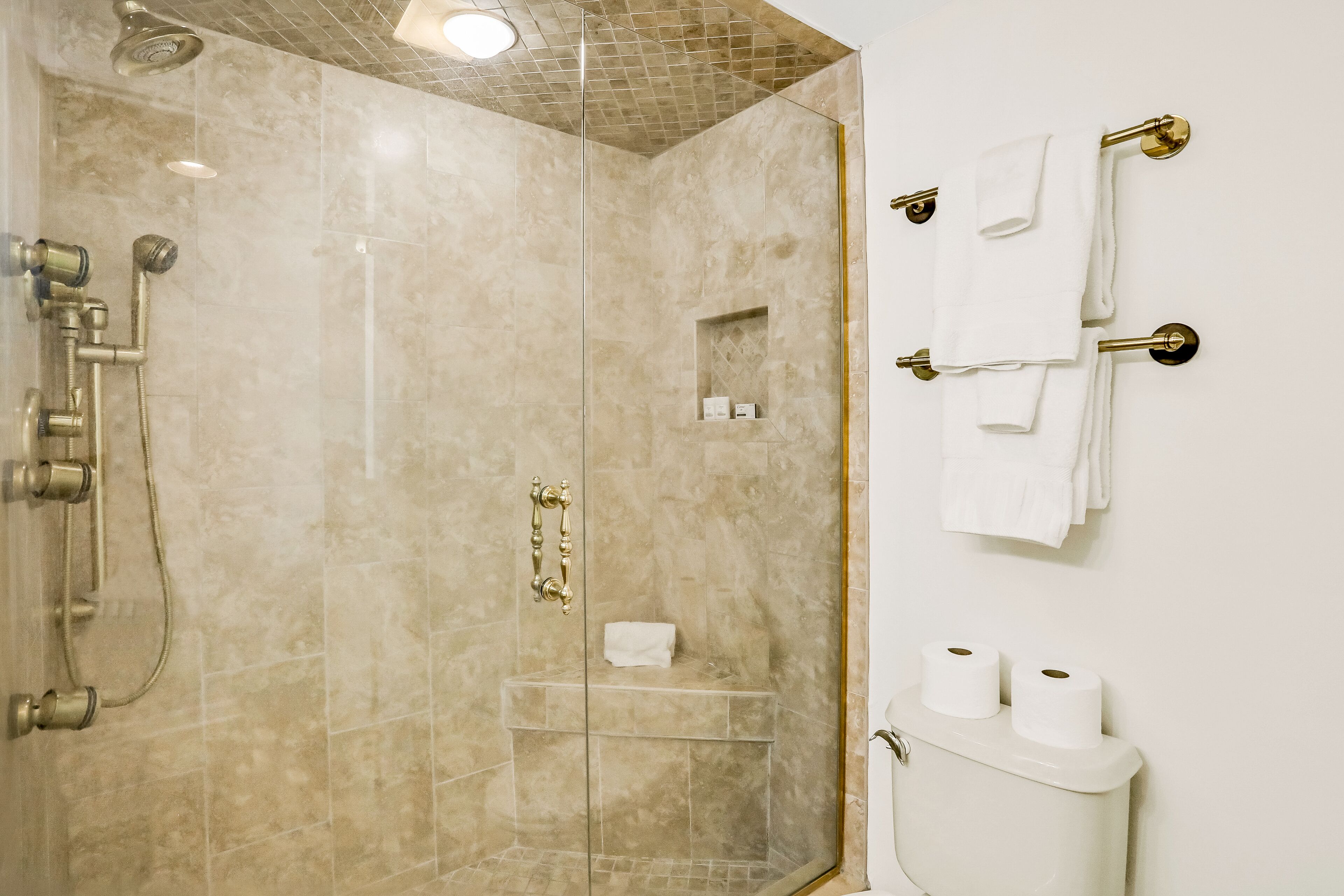 A bathroom with a glass-enclosed shower, a toilet with two rolls of toilet paper, and a towel rack with several white towels.