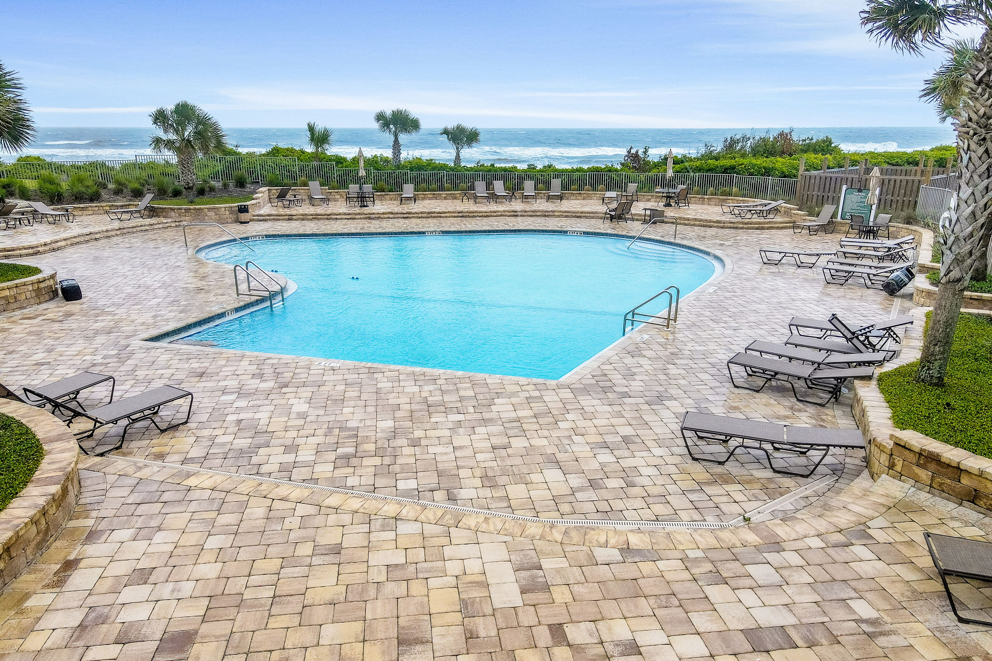 A pool area with a curved pool, lounge chairs, and a view of the ocean.