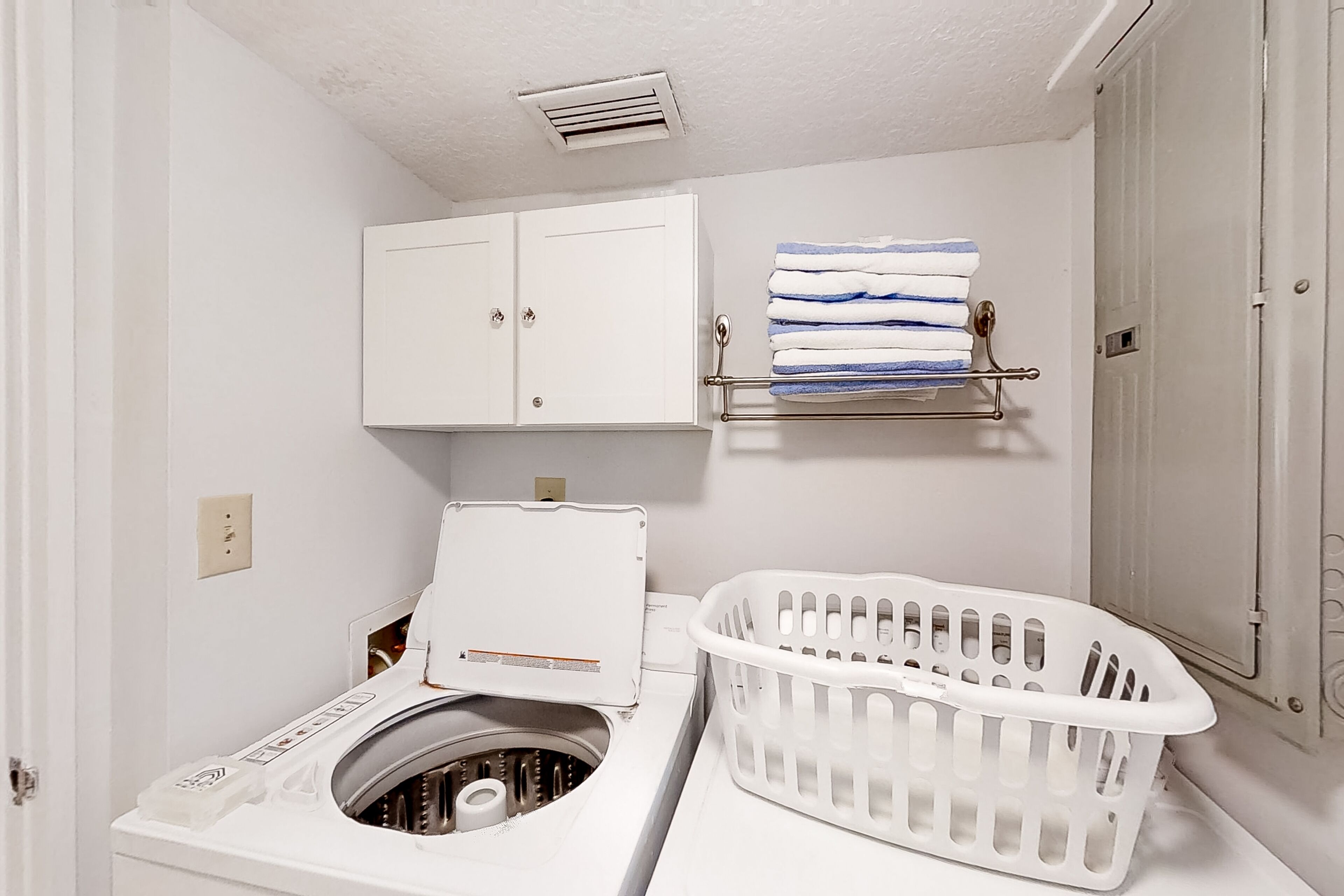 A compact laundry area with a washing machine, a drying rack, and a basket.
