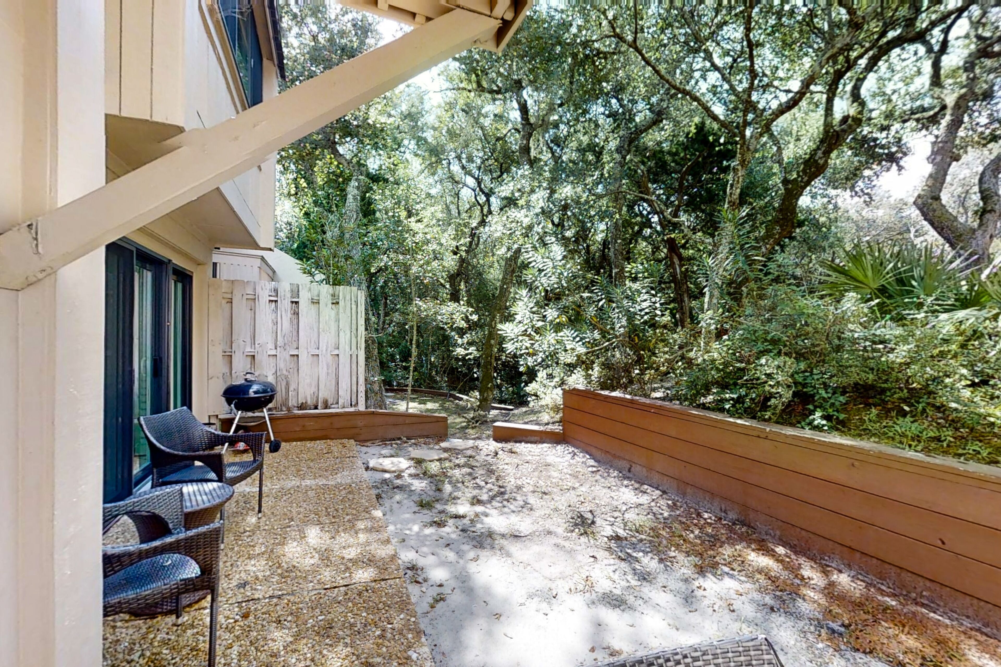 Ein Terrassenbereich im Freien mit Korbstühlen, einem Grill und einem Holzboden.
