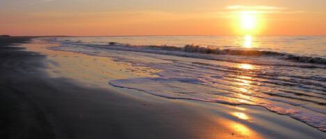 A beach at sunset with waves gently lapping the shore.