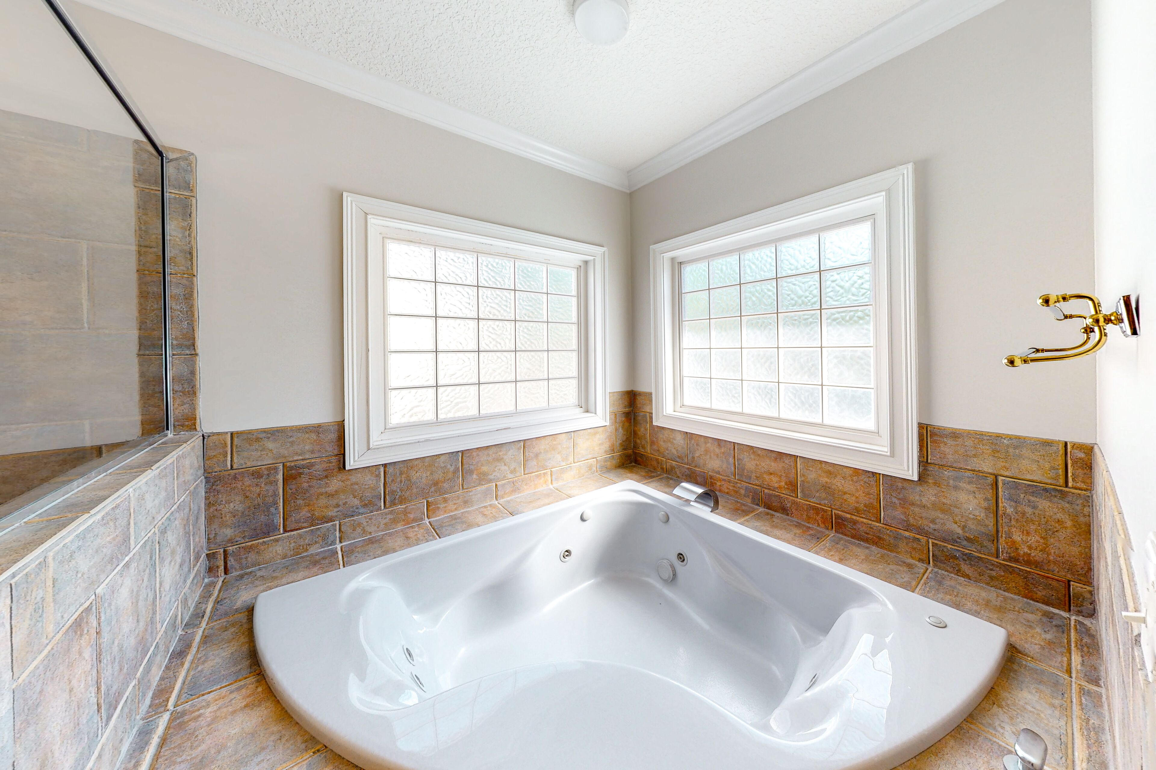 A modern bathroom with a freestanding bathtub, two windows with frosted glass, and a stone-tiled wall.