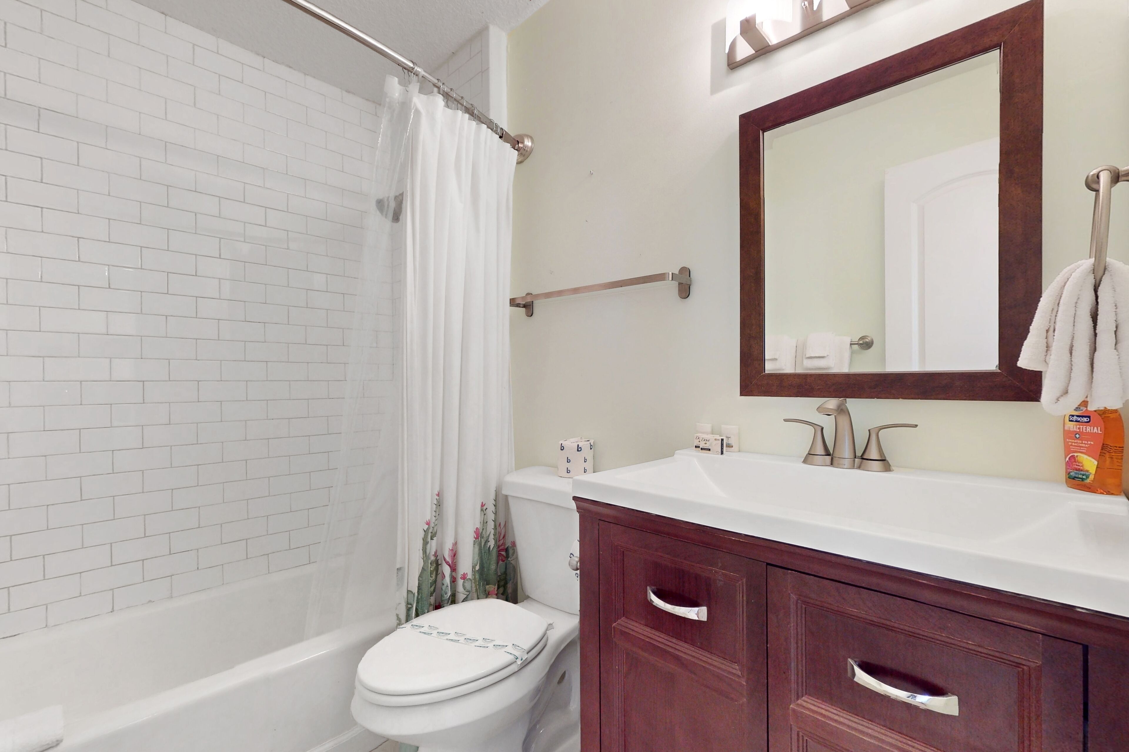 A bathroom with a white toilet, a bathtub, a shower curtain, a wooden vanity with a mirror, and toiletries on the sink.