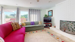 A living room with a sofa, TV, fireplace, and a ceiling fan. - Ocean Paradise Bright Home With Spacious Deck, Beach Access, Central AC & Wifi (St. Augustine)