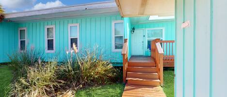 A turquoise building with a wooden staircase leading to a door.