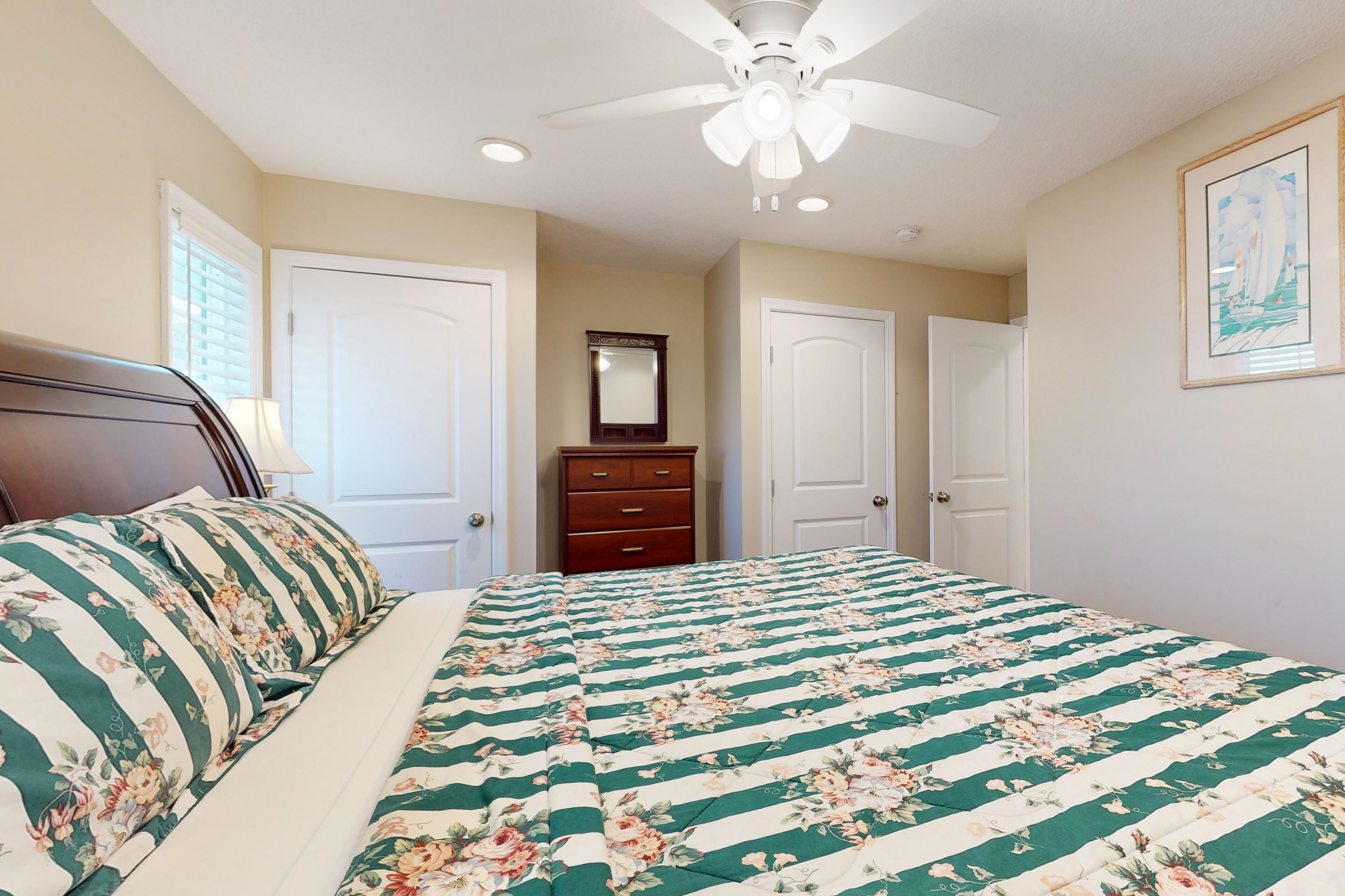 A bedroom with a bed, a dresser, a ceiling fan, and a framed picture on the wall.