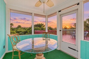 A glass-top table with chairs in a room with large windows and a view of the sunset. - Ocean Paradise Bright Home With Spacious Deck, Beach Access, Central AC & Wifi (St. Augustine)