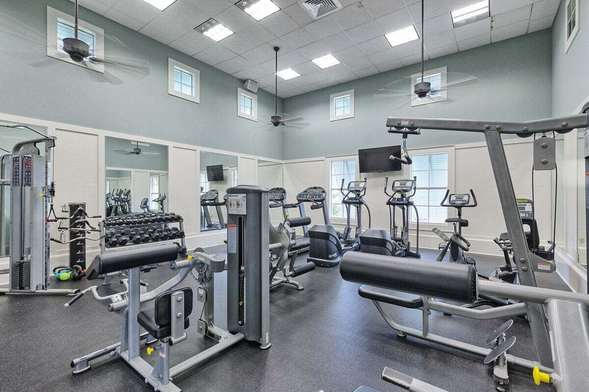 Un gimnasio con diverso equipo de ejercicio, ventanas amplias y ventiladores de techo.