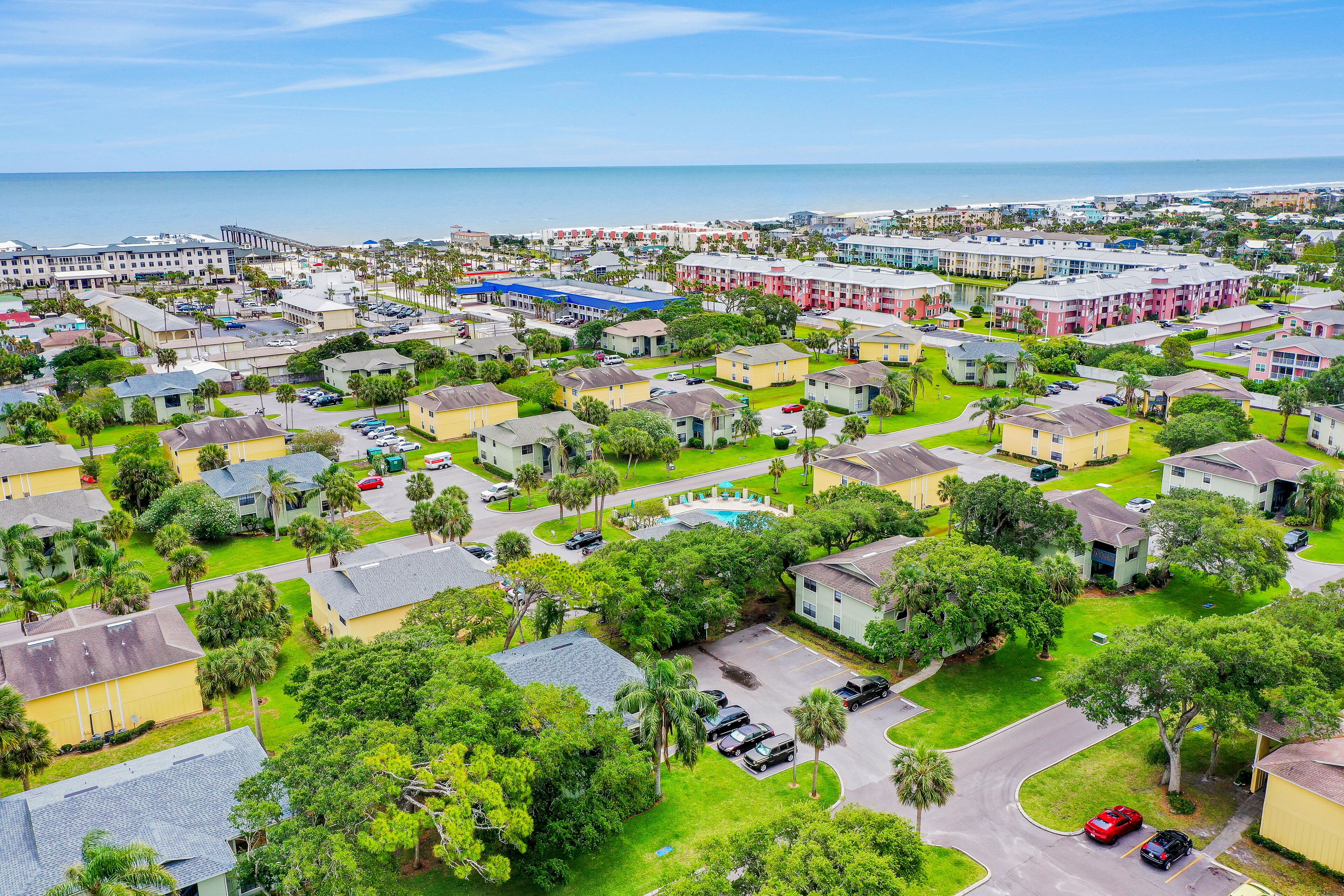 A residential area with multiple two-story houses, a swimming pool, and a beach in the background.