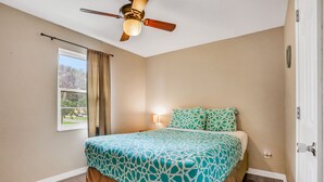 A bedroom with a bed, a ceiling fan, a window with curtains, and a nightstand with a lamp. - Charming Condo w/ Pool 500 Yards to Beach, Near Lighthouse & Downtown (St. Augustine)