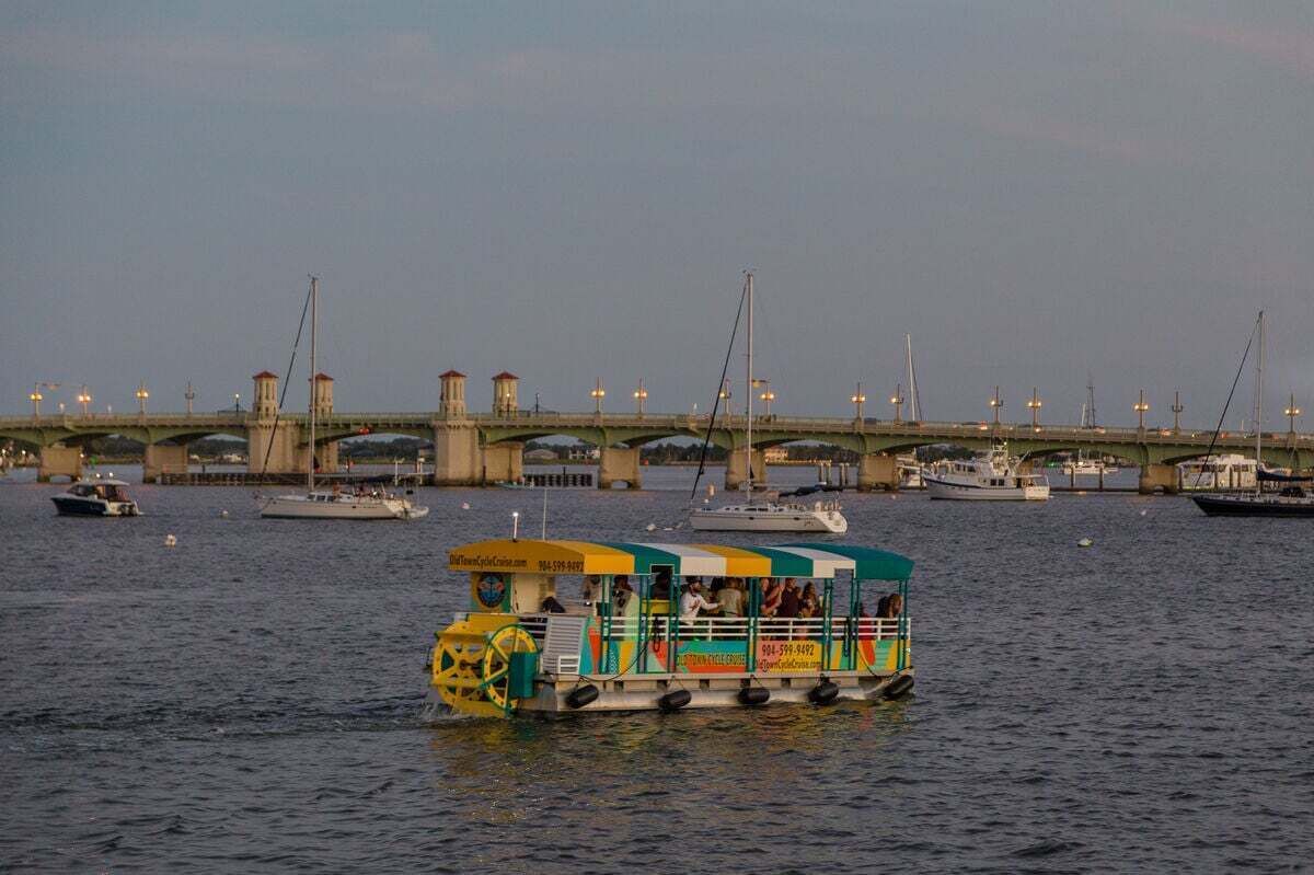 A riverboat with passengers, a bridge in the background, and several boats.