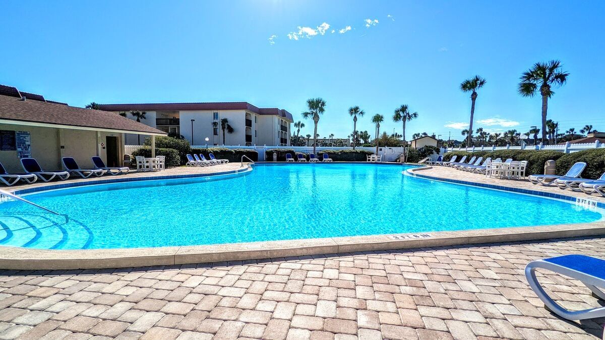 A swimming pool with lounge chairs and palm trees in the background.