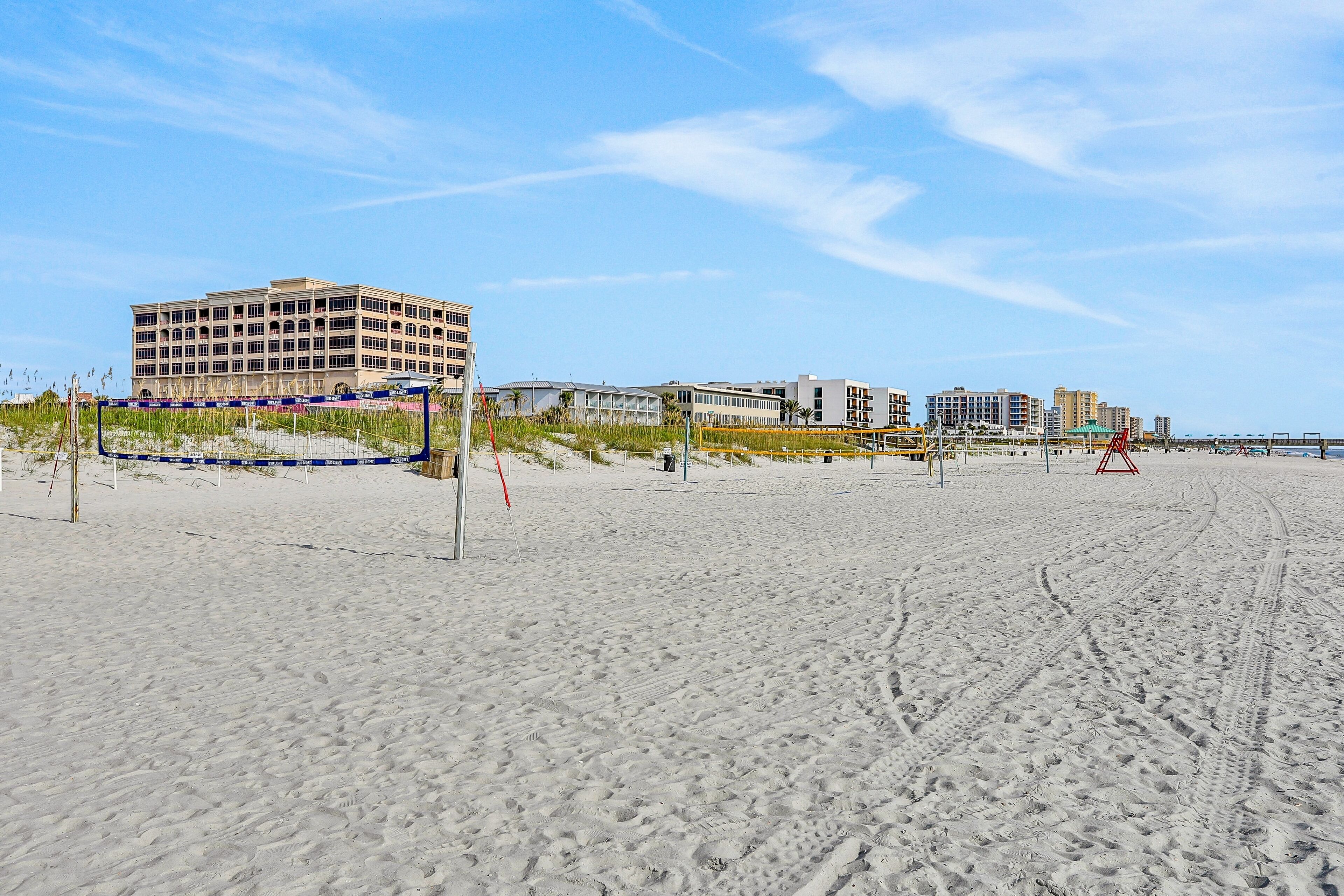 A sandy beach with a volleyball net and a building in the background.