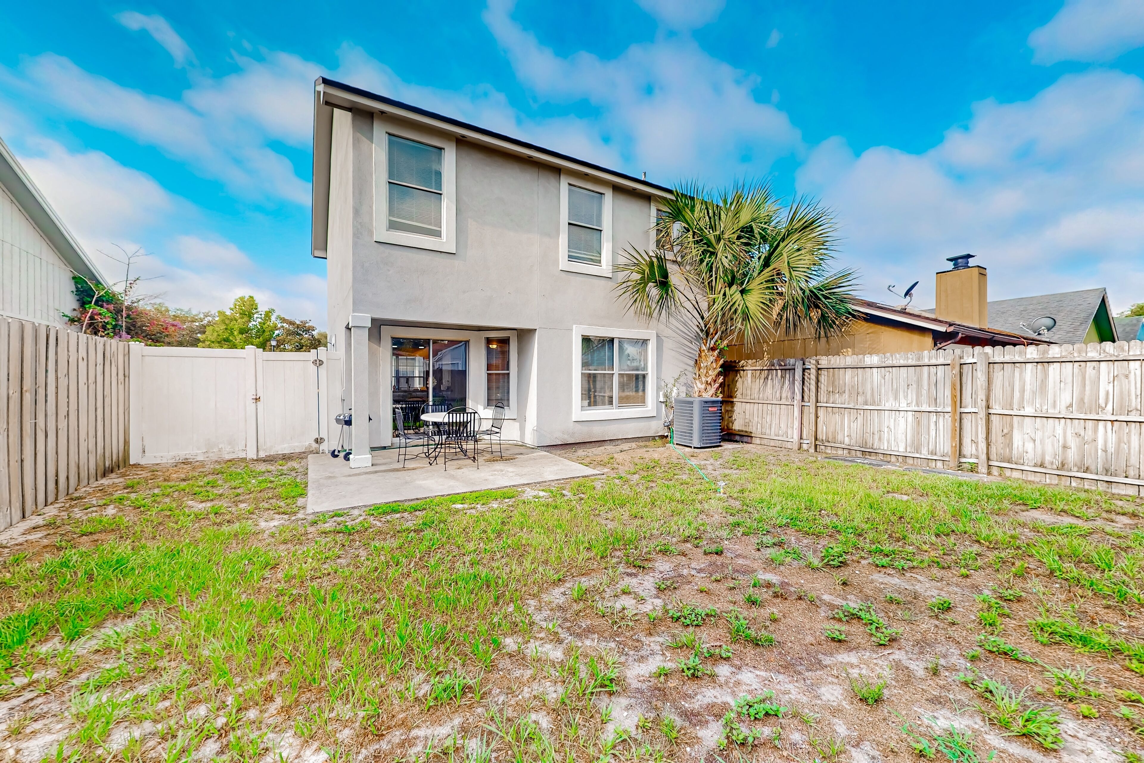 A two-story house with a patio, a wooden fence, and a palm tree.