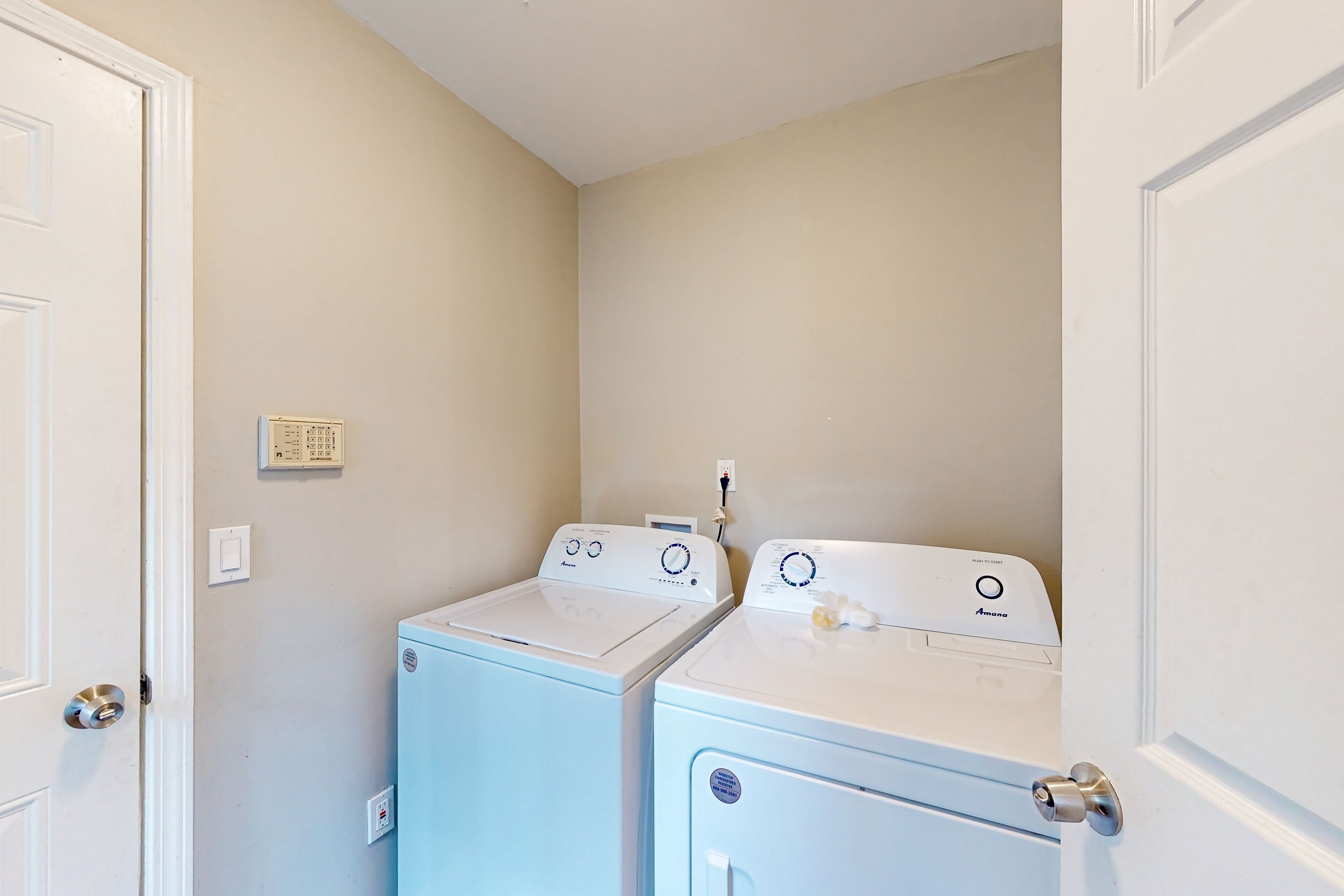 A laundry room with two stacked washing machines, a door, and a light switch on the wall.