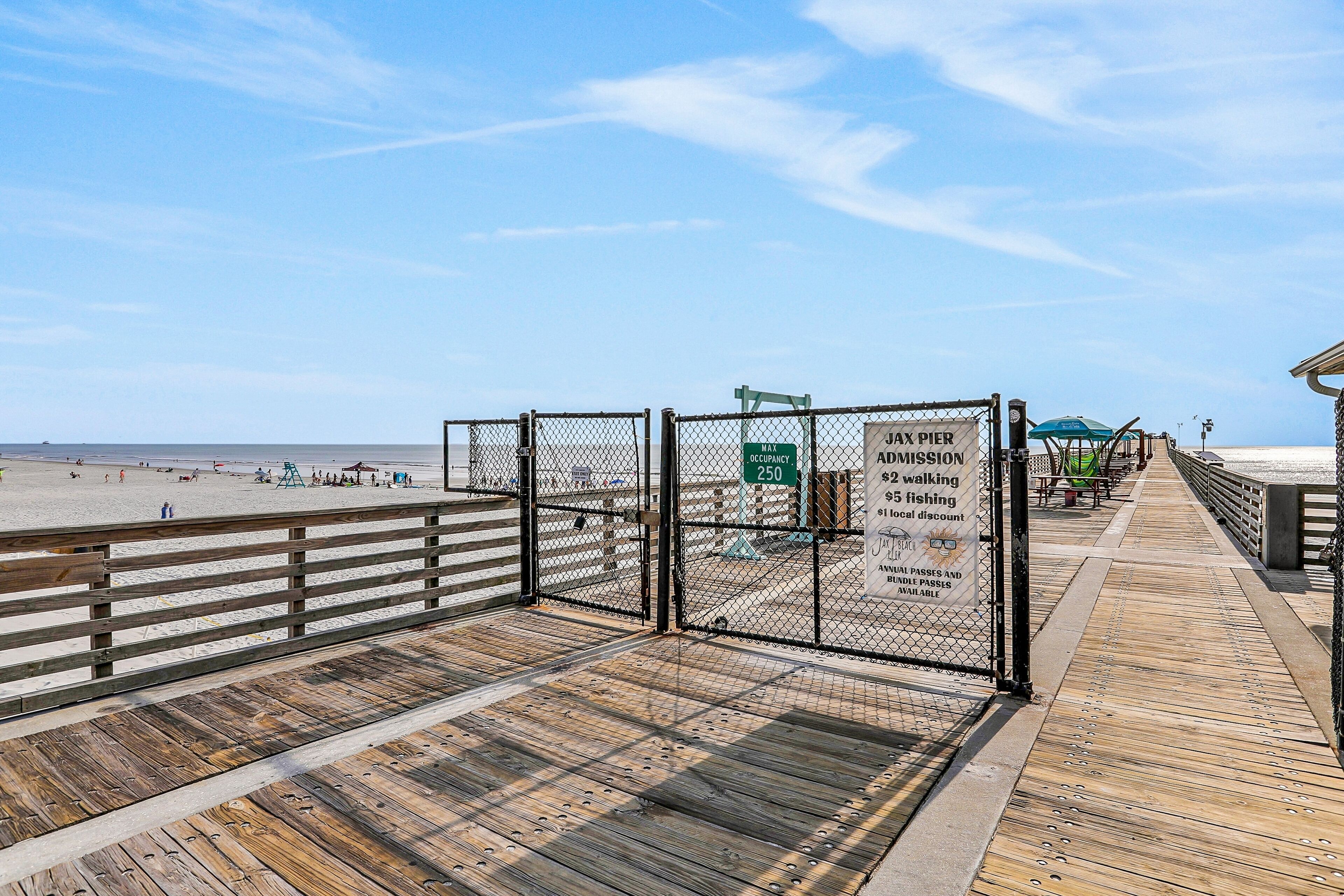 A wooden boardwalk leading to a beach with a fenced area and a sign indicating a maximum occupancy of 250.
