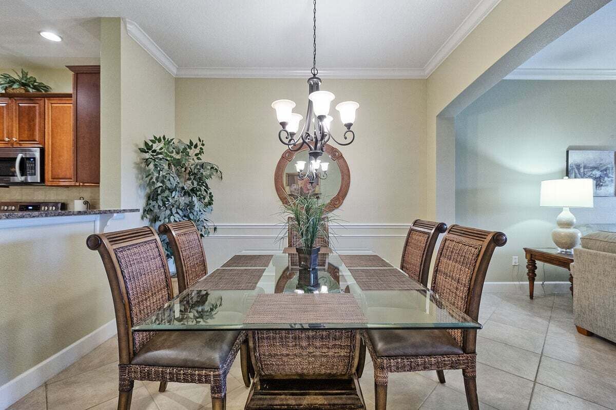 A dining area with a glass-top table, wicker chairs, a chandelier, and a potted plant.