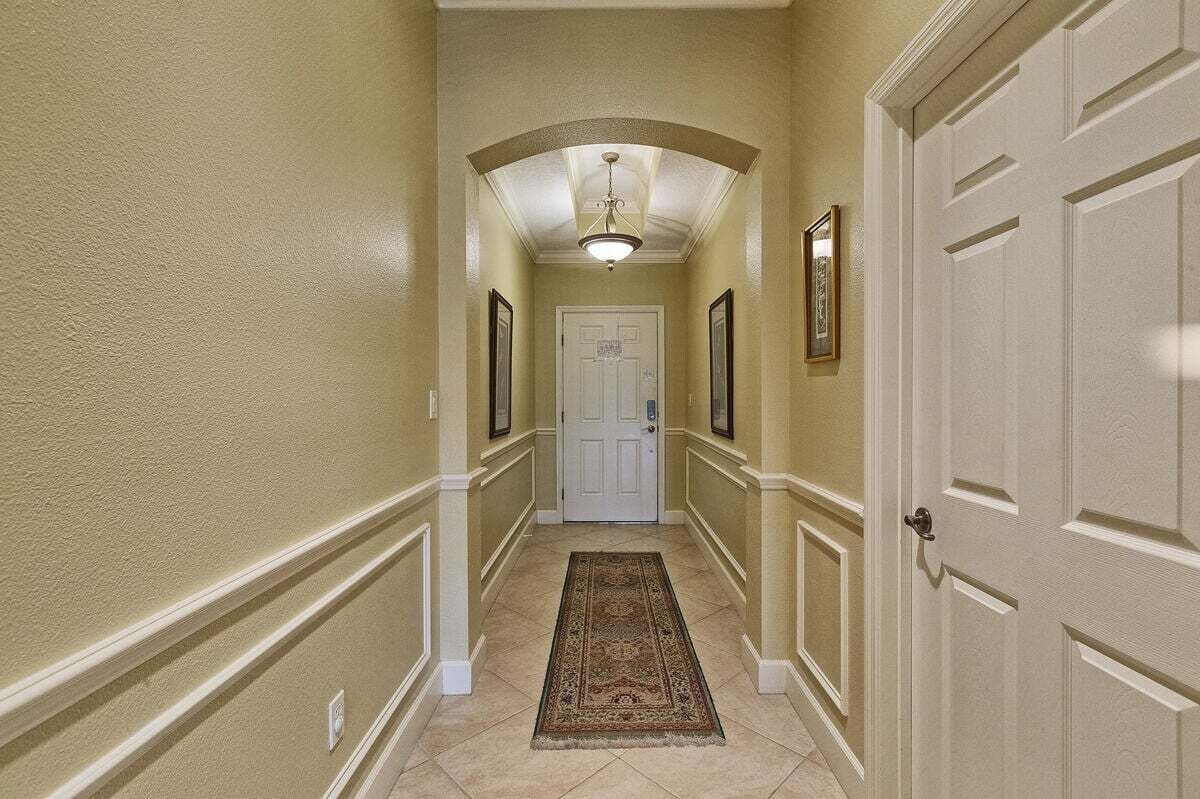 A hallway with a white door at the end, framed pictures on the walls, and a patterned rug on the floor.