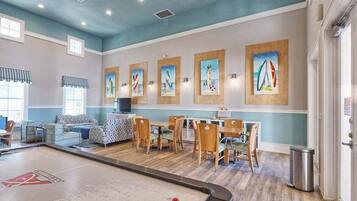 A pool table in a room with a blue ceiling, wooden chairs, and artwork on the walls.