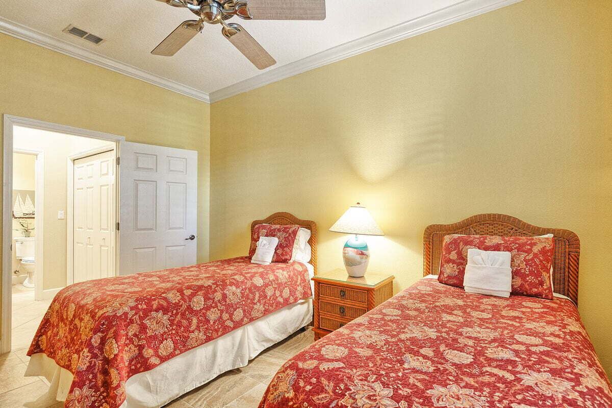 A room with two beds, a ceiling fan, a nightstand with a lamp, and a door leading to another room.