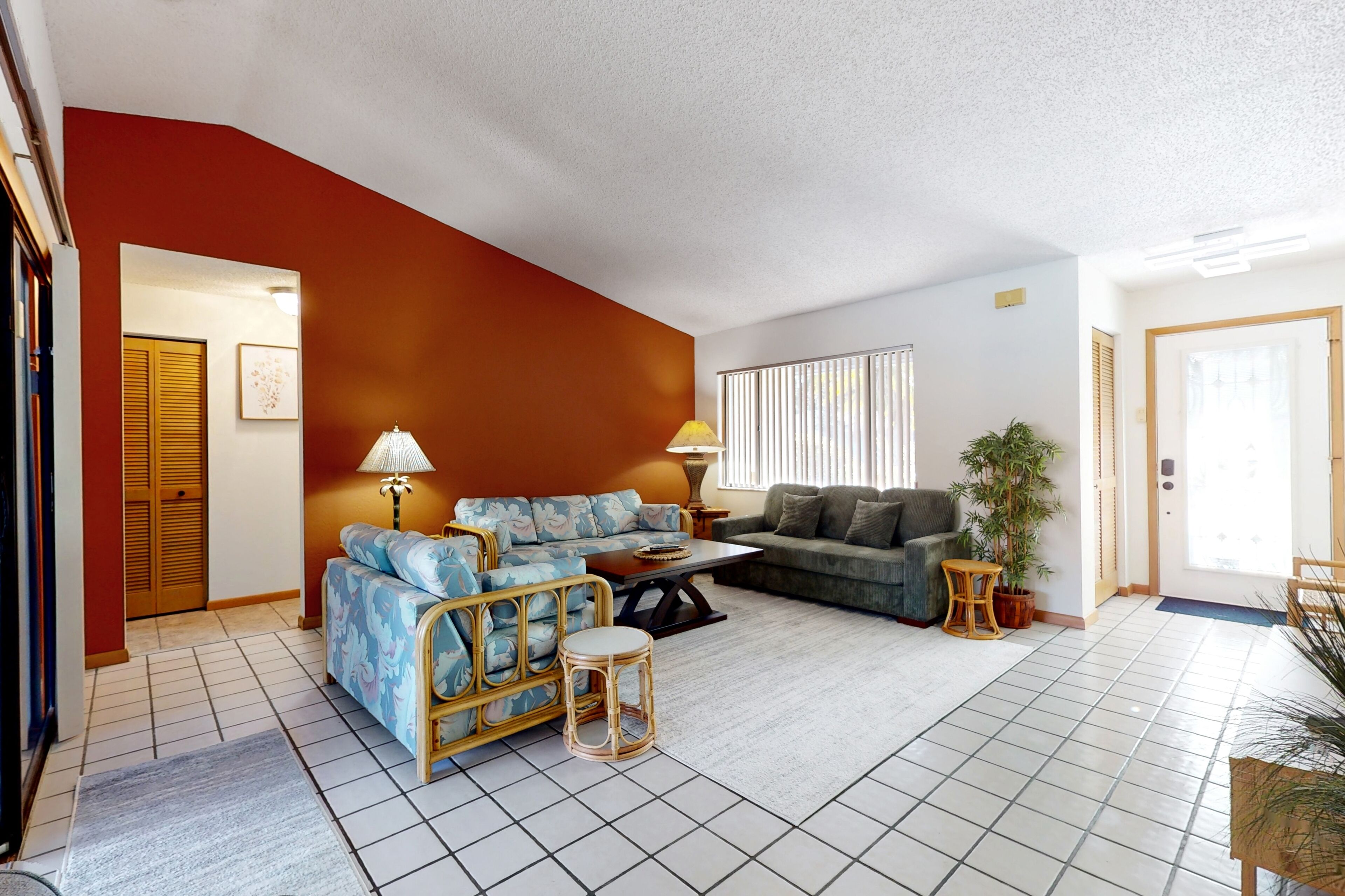 A living room with a sofa, a coffee table, and a lamp. There is a door and a window with blinds.