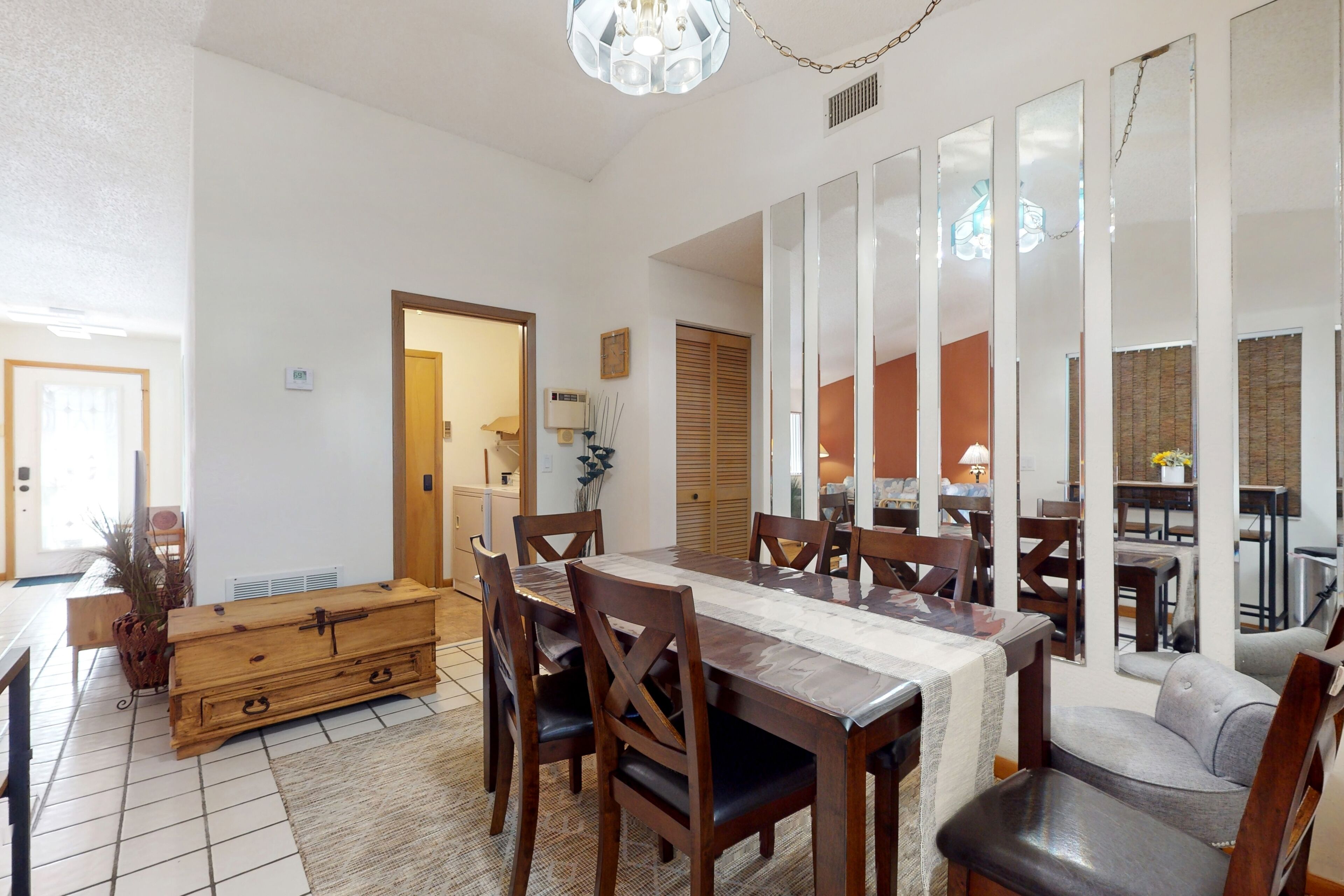 Zona pranzo con tavolo e sedie in legno, una panca e un grande specchio a parete.