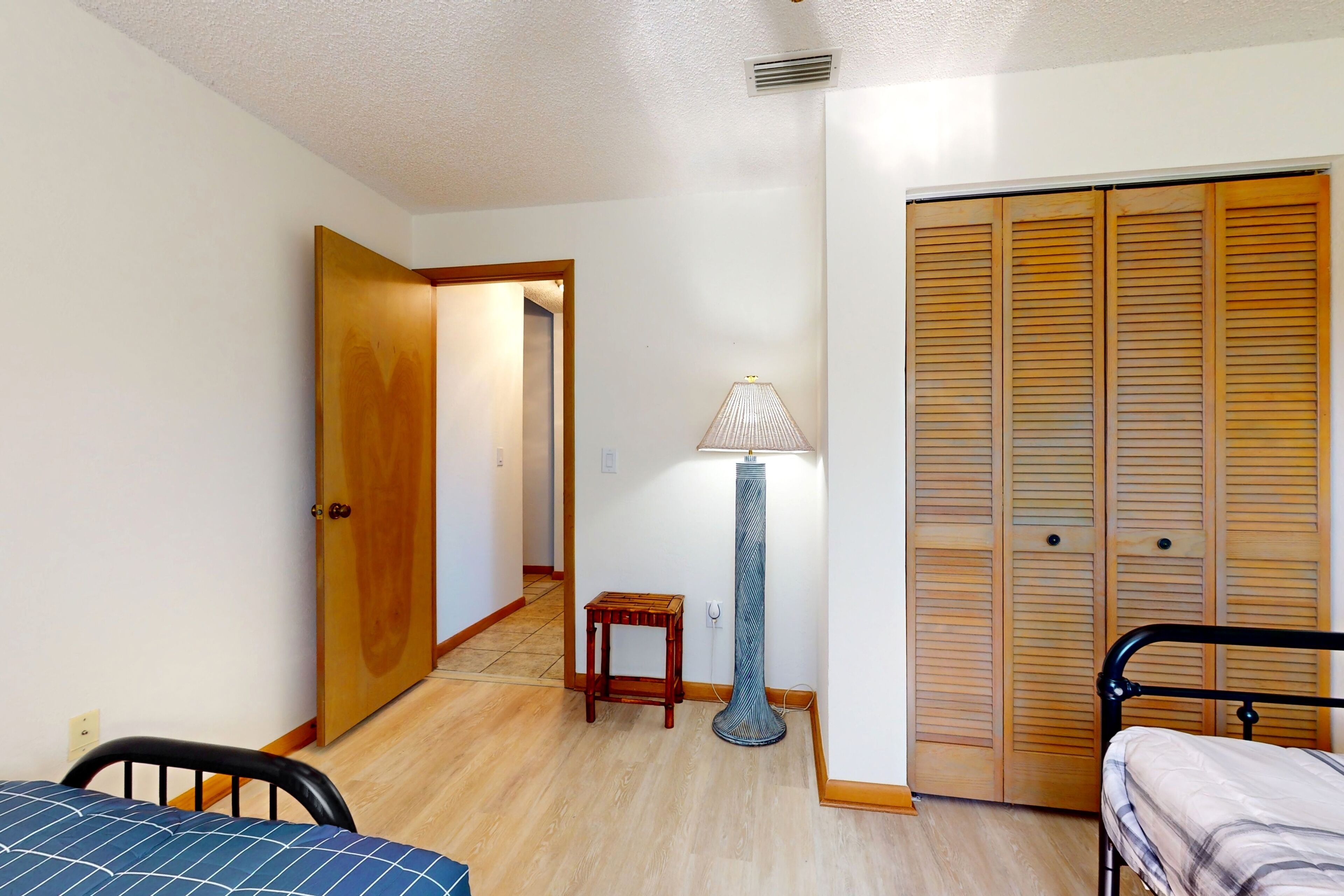 A bedroom with a bed, a nightstand, a lamp, a wooden door, and a closet with sliding doors.