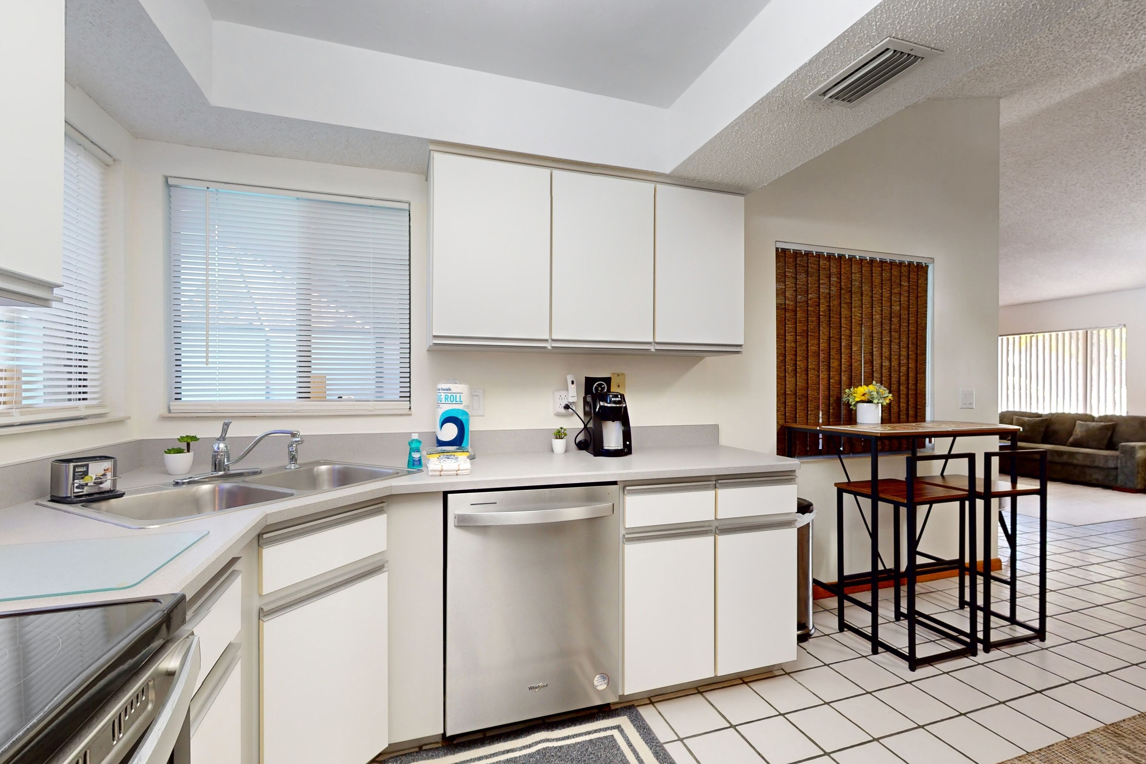 A compact kitchen with a built-in dishwasher, a coffee maker, and a small dining area with a table and chairs.