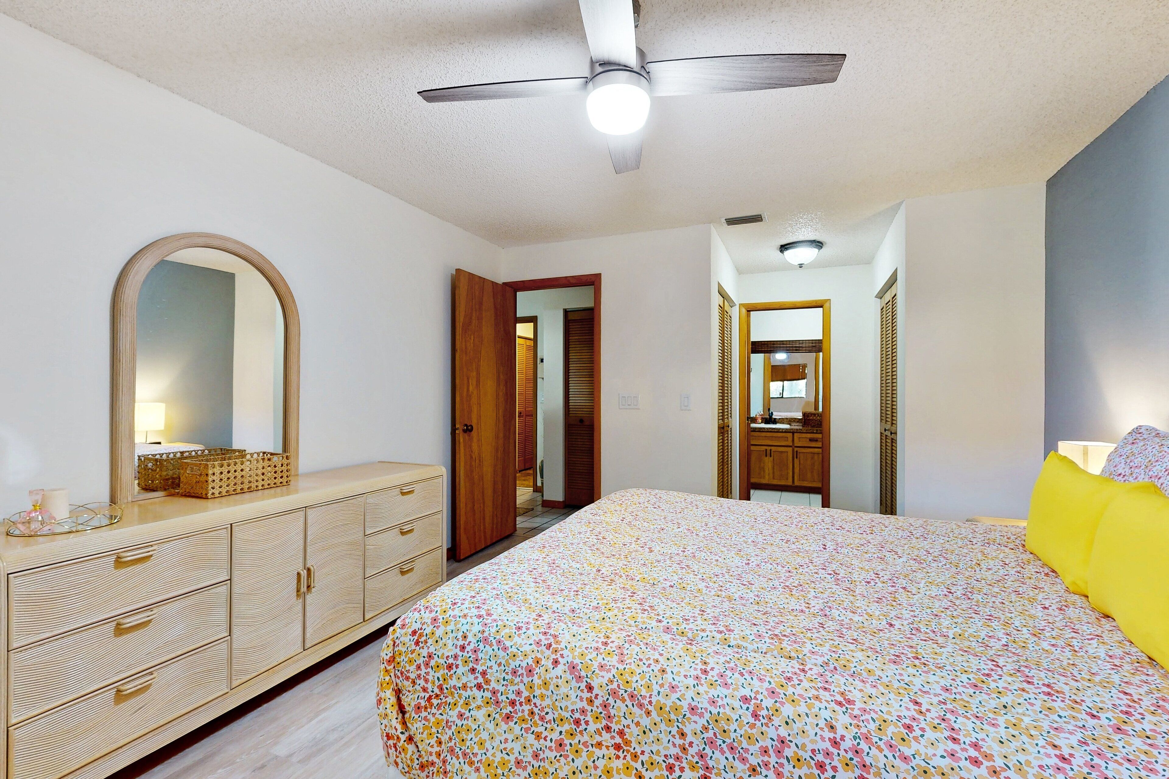 Une chambre à coucher avec un lit, une commode, un miroir et un ventilateur de plafond.
