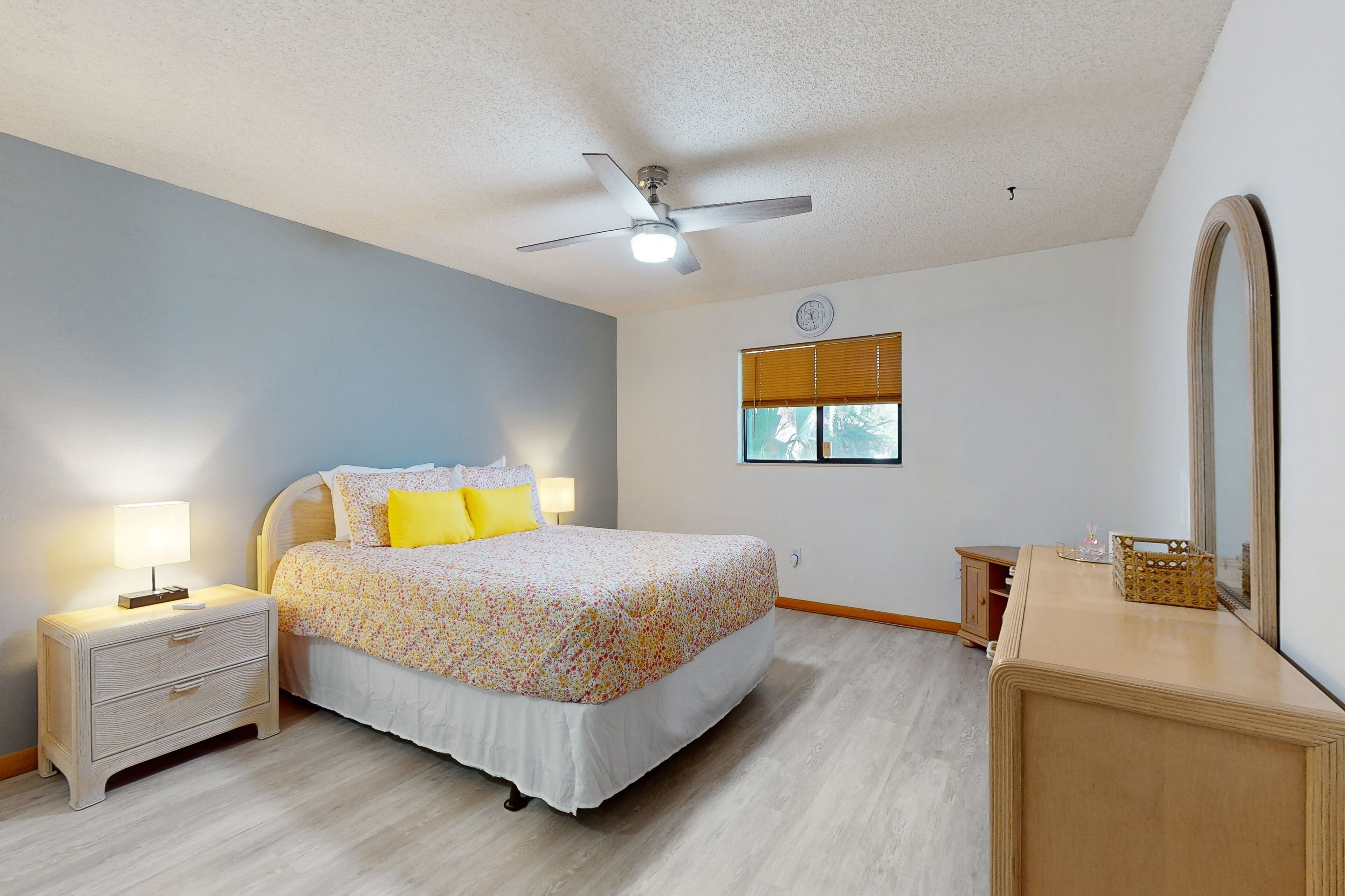 A bedroom with a bed, nightstands, a dresser, a ceiling fan, a window with blinds, and a mirror.
