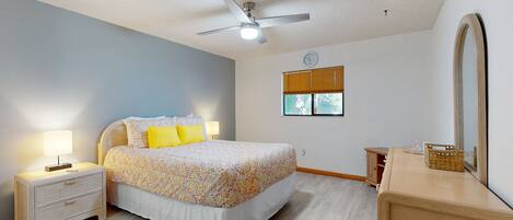 A bedroom with a bed, nightstands, a dresser, a ceiling fan, a window with blinds, and a mirror.