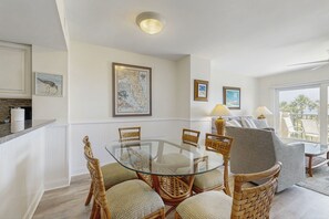 A dining area with a glass table surrounded by wicker chairs, a sofa, and framed artwork on the walls. - Beautiful Amelia Island Townhome With Pool & Tennis, Central AC (Fernandina Beach)