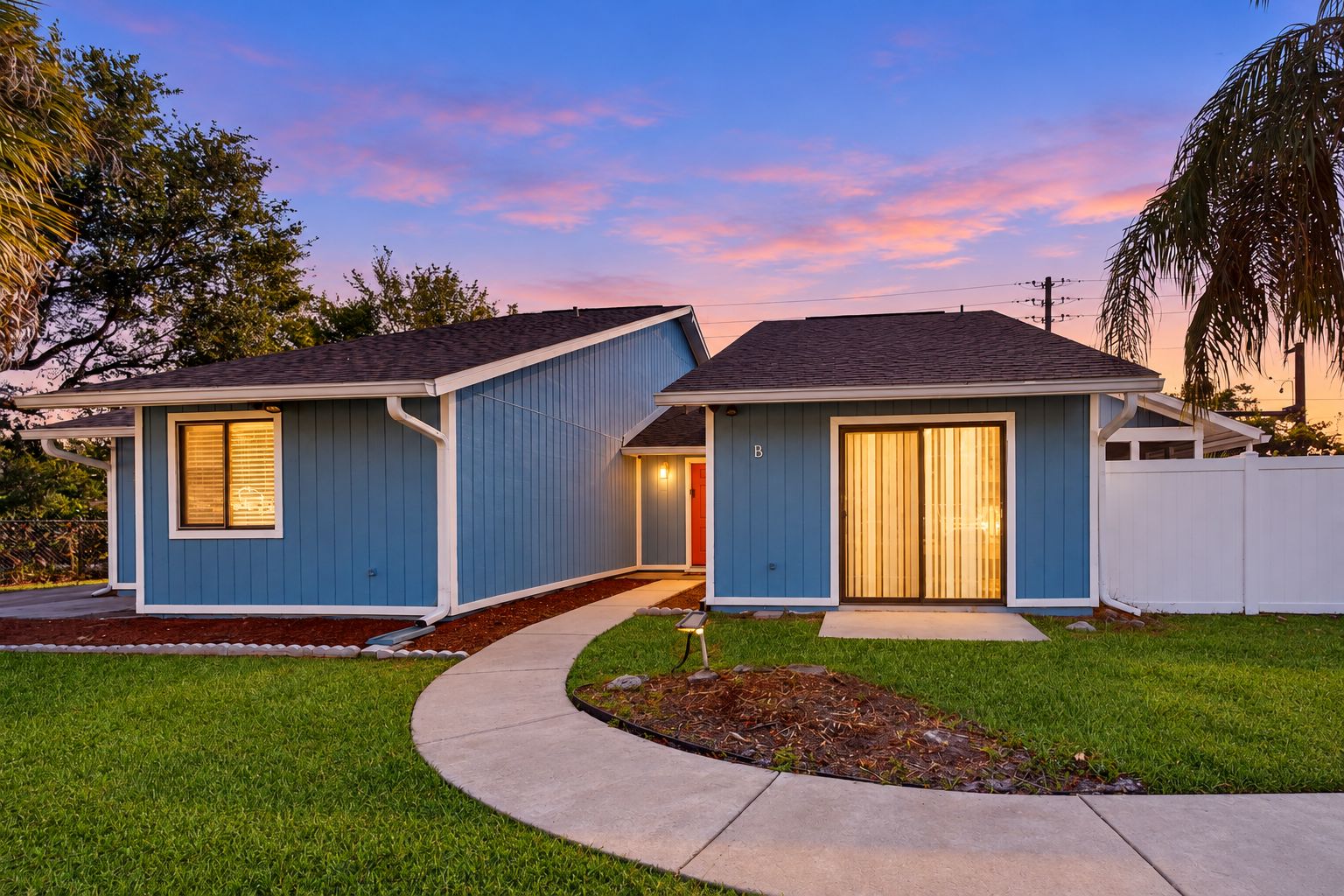A two-story residential house with a blue exterior, a front yard with a curved pathway, and a white fence.