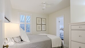 A bedroom with a bed, a dresser, a lamp, and a window with blinds. - Bright 1940s Beach Cottage With Cabana Plus Private Pool (St. Augustine)