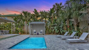 A swimming pool with lounge chairs and a covered seating area surrounded by tropical plants. - Bright 1940s Beach Cottage With Cabana Plus Private Pool (St. Augustine)