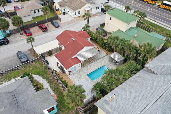 An aerial view of a residential area with houses, a swimming pool, and a street with vehicles. - Bright 1940s Beach Cottage With Cabana Plus Private Pool (St. Augustine)
