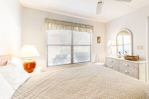 A bedroom with a large bed, two bedside lamps, a dresser with a mirror, and a window with blinds. - Bright & Sunny Oceanfront Getaway With Central AC & Pool (Fernandina Beach)