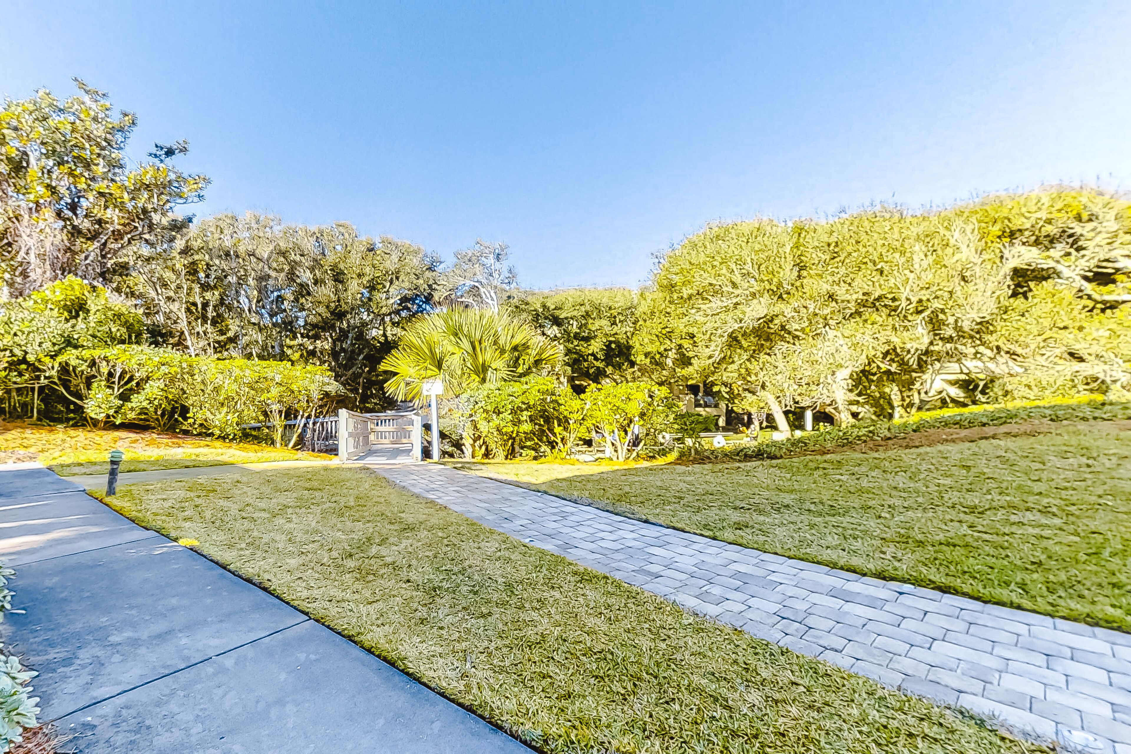 A paved pathway leading through a landscaped area with grass and trees.