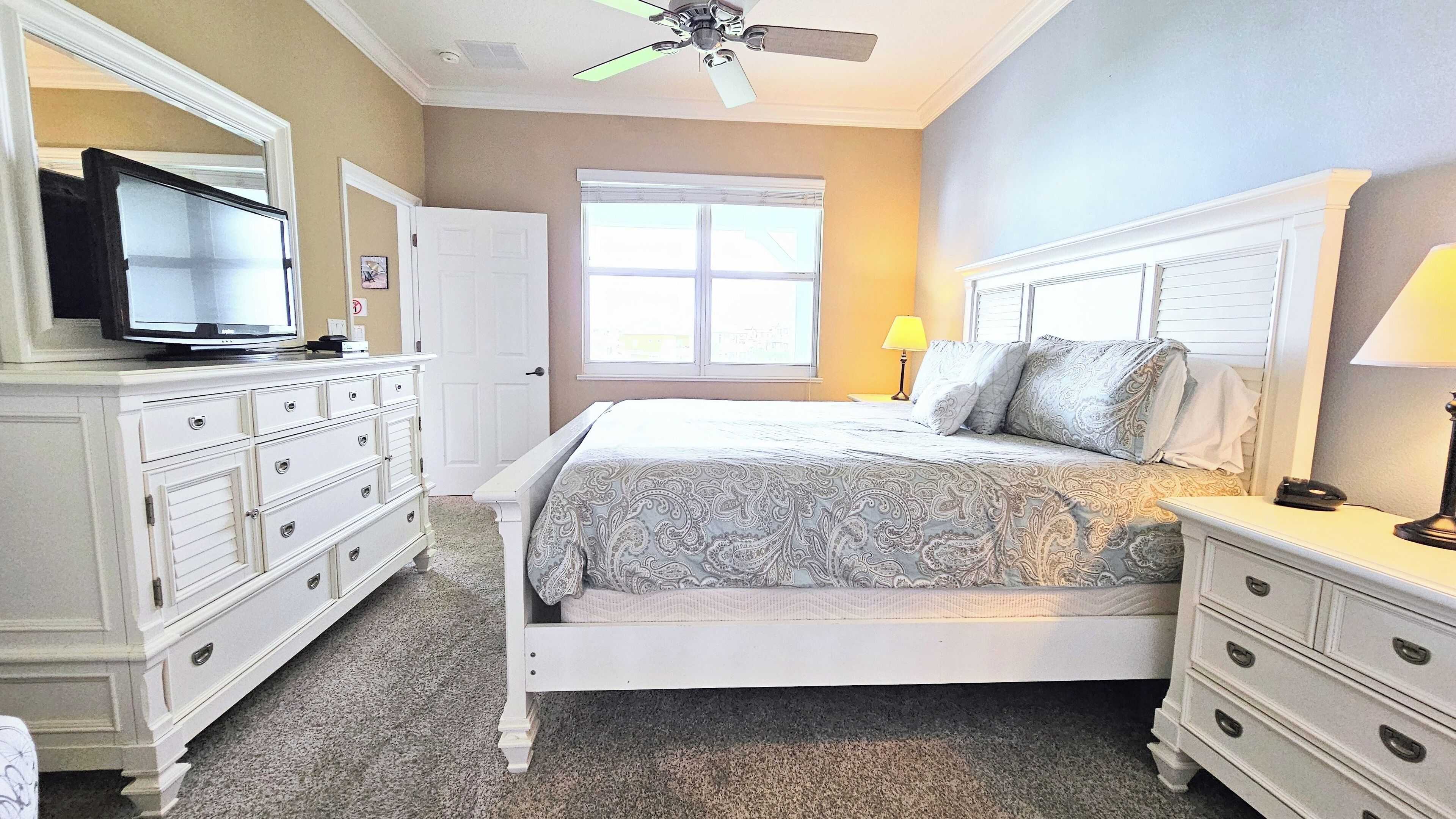 A bedroom with a bed, dresser, television, and a window with blinds.