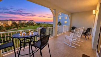 A balcony with a table and chairs, overlooking a golf course and a sunset.